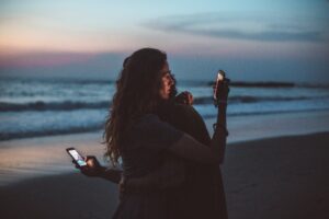 två personer surfar på sina telefoner på en strand